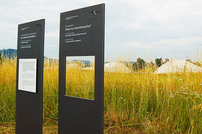 Das Bild zeigt zwei Infotafeln am Rande einer Wiese auf der Rückseite des Zentrums Paul Klee