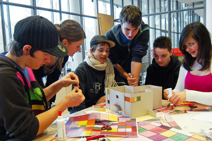 Sechs Schüler, welche gemeinsam ein Modell aus Karton mit farbigen Quadraten bekleben