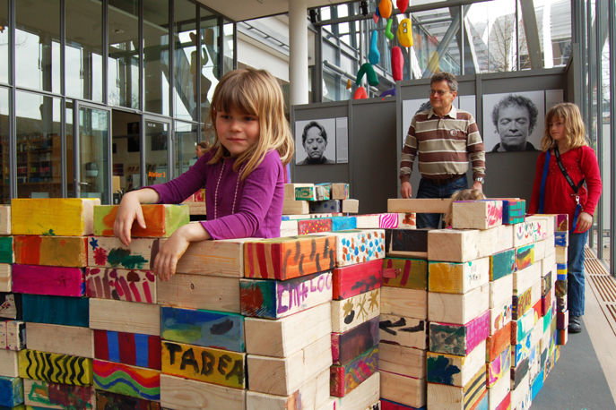 Zwei Kinder mit ihrem Vater welche aus Holzklötzen ein Haus gebaut haben