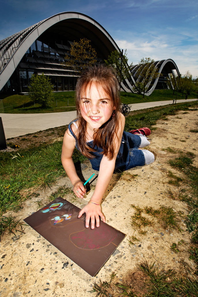 Ein Mädchen, dass im Gras vor dem Zentrum Paul Klee eine Zeichnung gestaltet