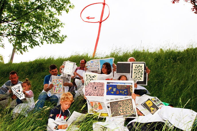 Erwachsene und Kinder lesen im Gras vor dem Zentrum Paul Klee selbst gestaltete Zeitungen