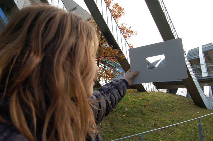 Ein Mädchen sieht durch einen Rahmen aus Karton auf das Zentrum Paul Klee