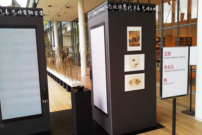 Foto aus der Ausstellung zeigt zwei schwarze Säulen an welchen Bilder und Papier zum beschreiben hängen